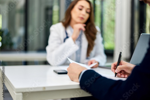 A male patient fills in his information while sitting with a female doctor in the office.