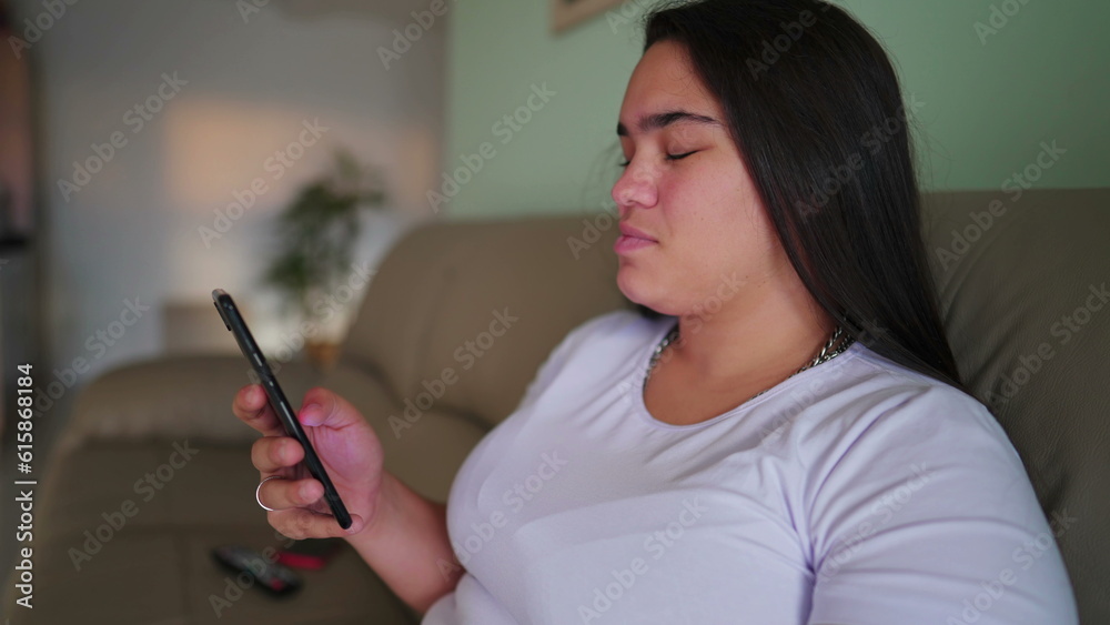 One diverse Brazilian young woman holding smartphone device sitting at home couch. South American adult girl in 20s browsing internet on phone One diverse Brazilian young woman holding smartphone device sitting at home couch. South American adult girl in 20s browsing internet on phone