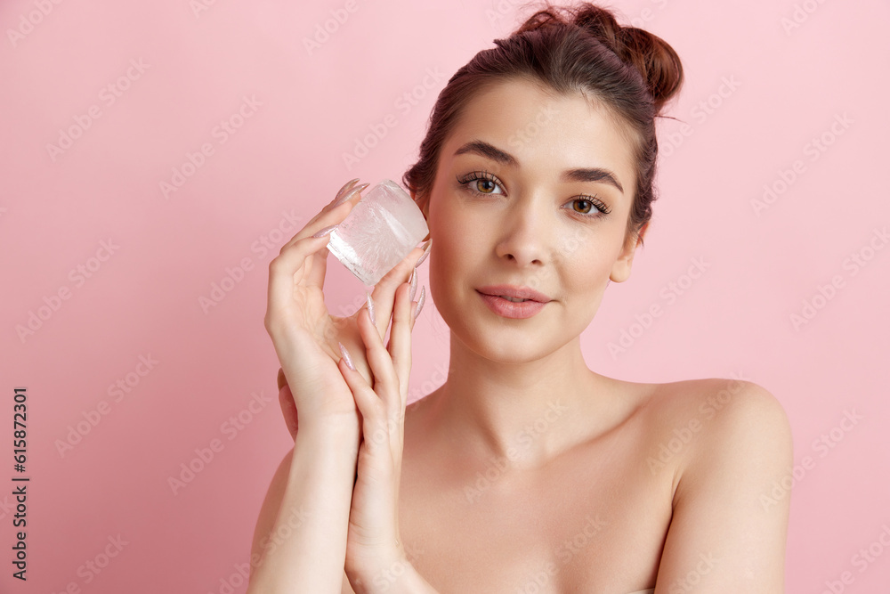 Young beautiful woman taking care after her perfect skin with ice cube over pink studio background. Refreshment and anti-wrinkle care. Concept of natural female beauty, skincare, cosmetology, health