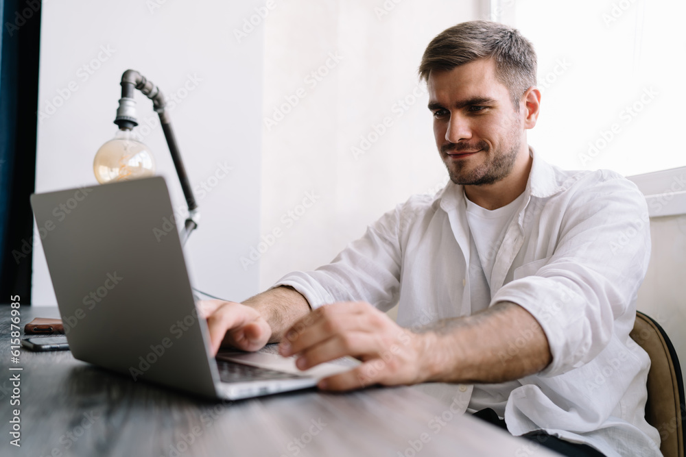 Cheerful man shopping online on laptop while sitting at table