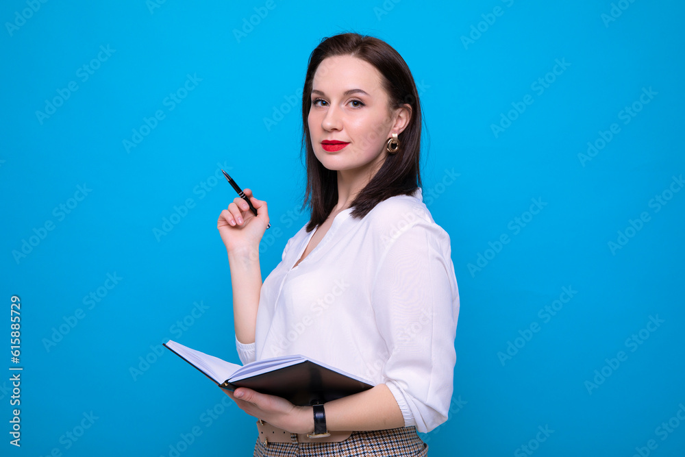 Young brunette woman with a diary and pen on a blue background Young brunette woman with a diary and pen on a blue background