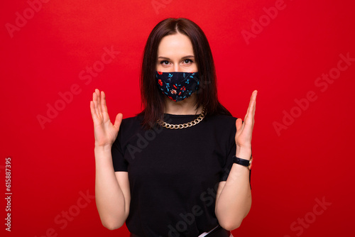 Portrait of a stylish young woman in a coloured protective mask on a red background