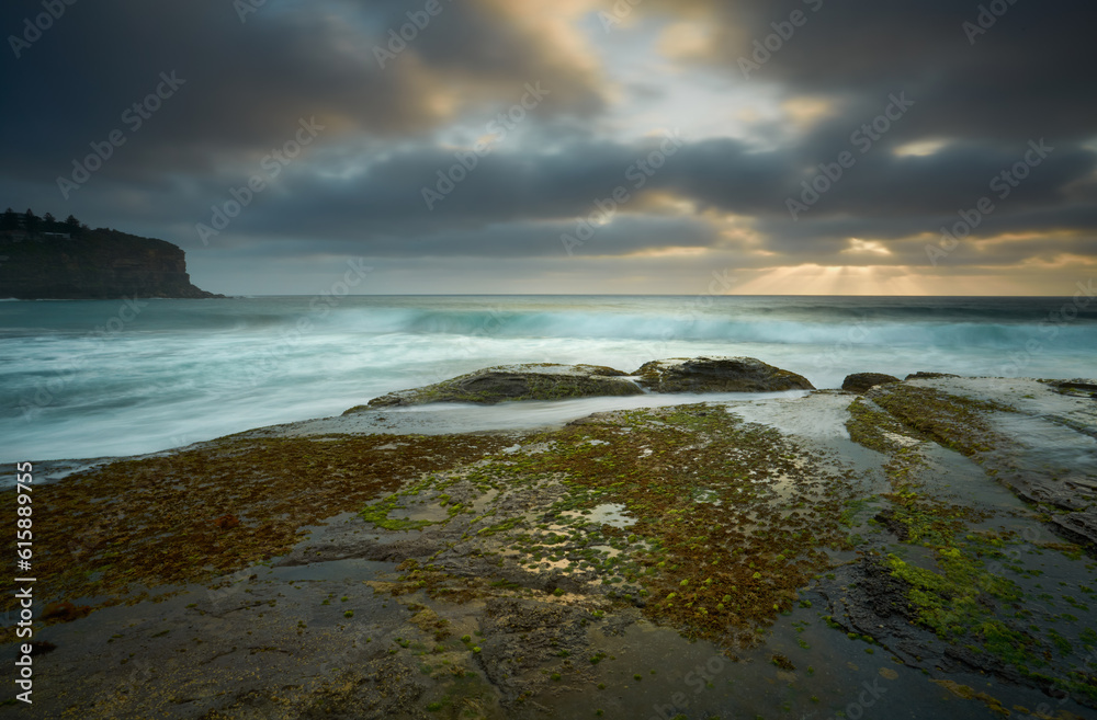 Moody clouds leave a small break for the sunrays to peak through on the low tidal rockshelf at Bilgola