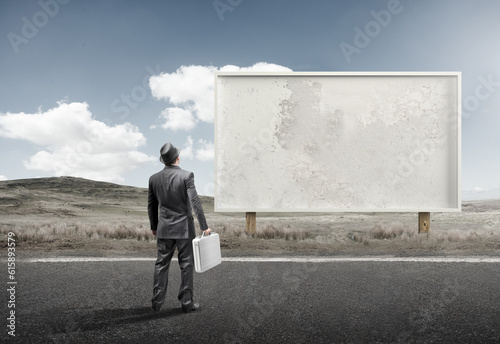 A business man standing and staring at a blank billboard advertisement.