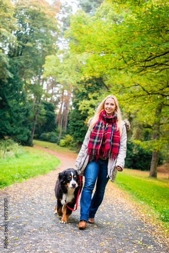 Woman walking the dog on leash in park on path covered with colorful fall foliage