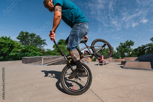 A middle-aged tattooed man is practicing an extreme sport in a skate park.