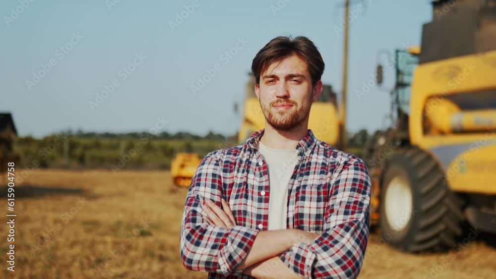 Portrait of proud harvester machine driver with hands crossed on chest. Farmer standing at his combine. Agronomist looking at camera. Rancher at harvesting work on stubble of harvested wheat field. Portrait of proud harvester machine driver with hands crossed on chest. Farmer standing at his combine. Agronomist looking at camera. Rancher at harvesting work on stubble of harvested wheat field.