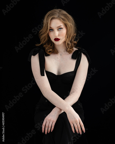 Beautiful redhead girl in black dress in front of black studio background