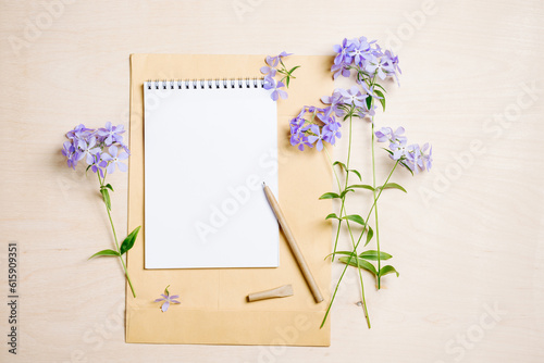 Summer mockup scene. Blank notebook, pen and blue flowers on a wooden background.