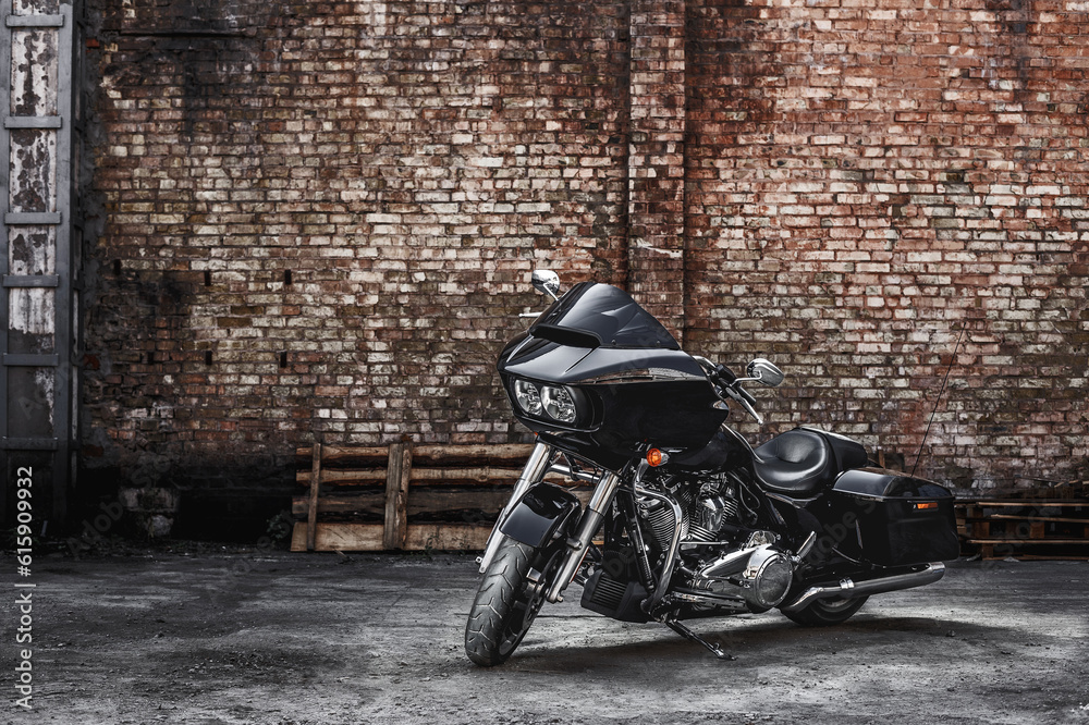 Modern black motorcycle stands against a brick wall background. Advertising poster image.
