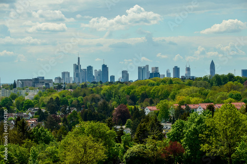 Frankfurt skyline behind some houses and green trees under cloudy summer sky