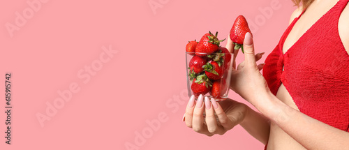 Fototapeta Naklejka Na Ścianę i Meble -  Young woman in red swimsuit holding glass of fresh strawberries on pink background. Banner for design