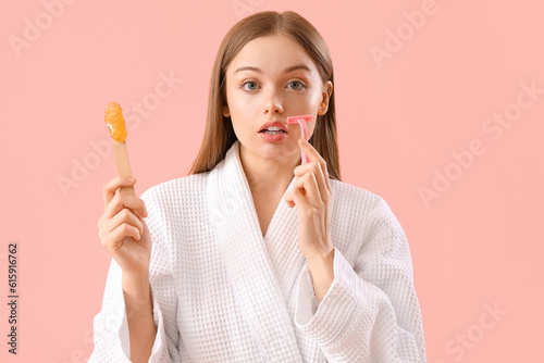 Young woman holding spatula with sugaring paste and razor on pink background photo