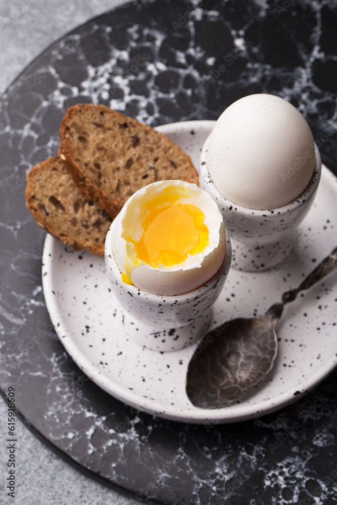 Two soft boiled eggs in eggcups with slice of bread on marble plate. Top view, close up Two soft boiled eggs in eggcups with slice of bread on marble plate. Top view, close up