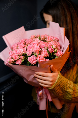 Young darkhair woman florist holding in hands large bouquet of fresh pink roses photo