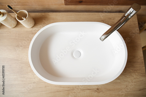 White sink with bath accessories on table near wooden wall photo