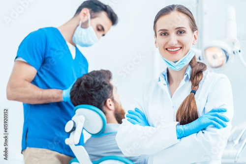 Portrait of a happy and confident female dentist wearing sterile white coat and surgical gloves  while looking at camera in the dental office of a modern clinic with reliable specialists