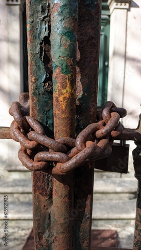 The old rusty gate is closed and wrapped with a thick steel chain with a lock