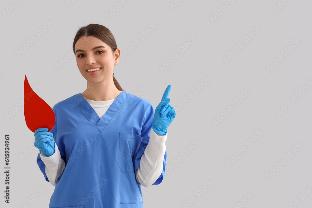 Female nurse with paper blood drop pointing at something on light background Female nurse with paper blood drop pointing at something on light background