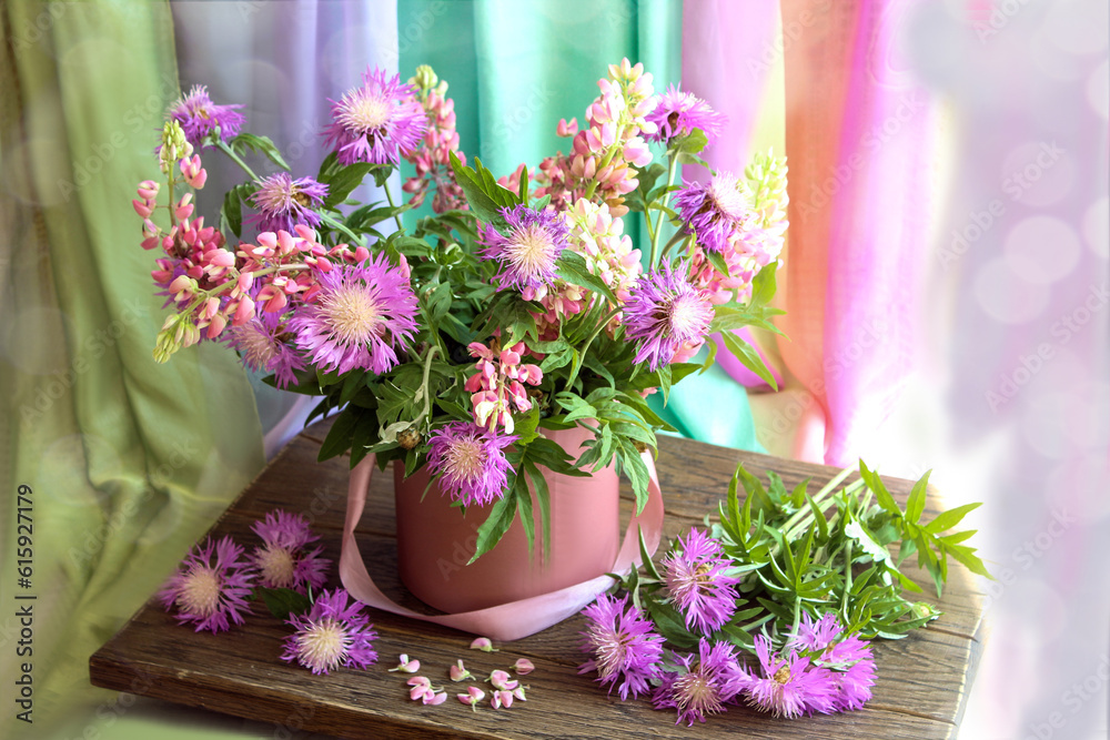 Summer bouquets: a bouquet of purple cornflowers and lupins on a wooden table on a colorful background, space for text Summer bouquets: a bouquet of purple cornflowers and lupins on a wooden table on a colorful background, space for text