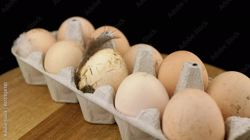 Brown Dirty Chicken Eggs in a Tray on a Rotating Wooden Desk, Black Background. Turning. Ten raw messy eggs with feathers stuck to them, chicken manure. Eco products. Protein. Cardboard box. Farming. Brown Dirty Chicken Eggs in a Tray on a Rotating Wooden Desk, Black Background. Turning. Ten raw messy eggs with feathers stuck to them, chicken manure. Eco products. Protein. Cardboard box. Farming.