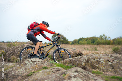 Fototapeta Naklejka Na Ścianę i Meble -  Cyclist in Red Riding the Bike on the Rocky Trail on the Sunset Sky Background. Extreme Sport and Enduro Biking Concept.