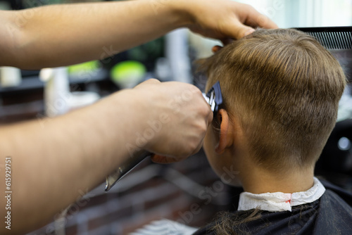 View from the back. The hairdresser cuts the hair on the boy's head with a machine in a beauty salon. The child calmly gives the hairdresser a haircut. © Александр Лебедько