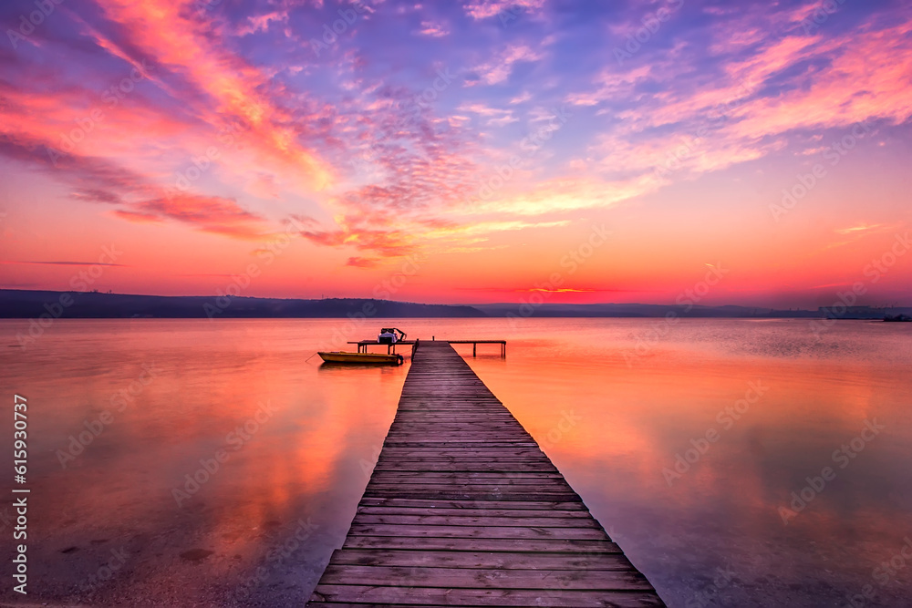 Exciting sunset at shore with wooden pier and boat