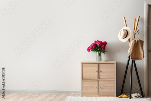 Vase of red peonies with coat rack and dresser near light wall