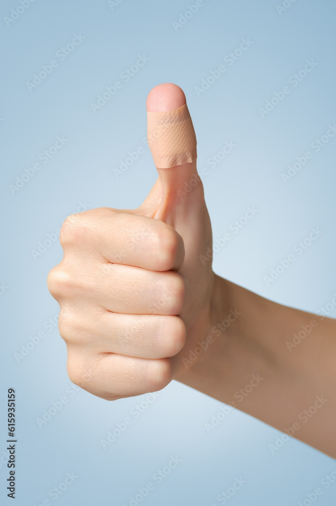 Female thumb with adhesive bandage on blue background