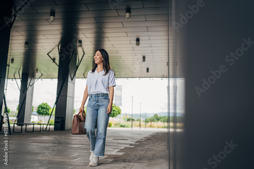 Pretty young Japanese business woman walking with bag in the office hallway
