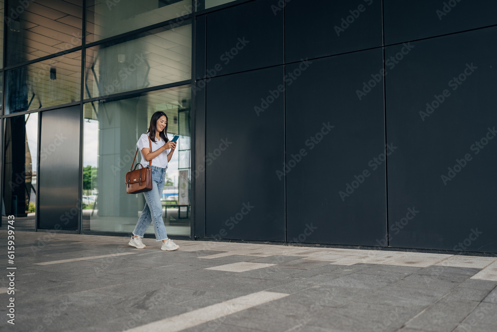 Young busy successful beautiful Japanese business woman, Japanese professional businesswoman holding cellphone using smartphone standing or walking on big city urban street outside Young busy successful beautiful Japanese business woman, Japanese professional businesswoman holding cellphone using smartphone standing or walking on big city urban street outside
