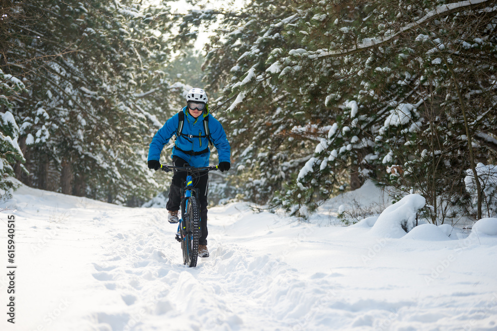 Cyclist in Blue Riding the Mountain Bike in the Beautiful Winter Forest Covered with Snow. Extreme Sport and Enduro Biking Concept.