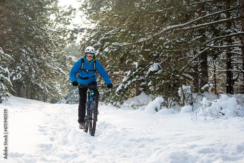 Cyclist in Blue Riding the Mountain Bike in the Beautiful Winter Forest Covered with Snow. Extreme Sport and Enduro Biking Concept.