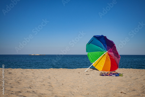 A colorful umbrella and a towel on a sunny golden send beach.