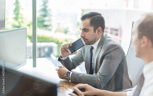 Image of two thoughtful businessmen looking at data on computer screens, solving business issue at business meeting in moder office.