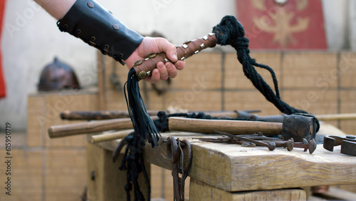 Roman soldier taking a whip from a table with torture instruments. Focused detail