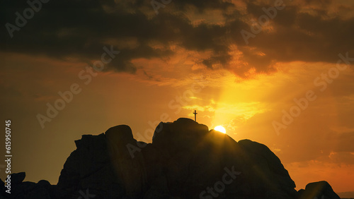 Silhouette of the Cross on mountain at sunset with rays