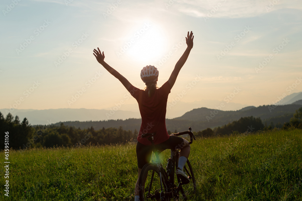 Happy female road racing cyclist in joy, with arms raised above her head, after successfully reaching a goal Happy female road racing cyclist in joy, with arms raised above her head, after successfully reaching a goal