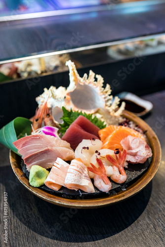 Selective focus decorated sashimi set in a bowl with ice and conch shell near the chef bar.