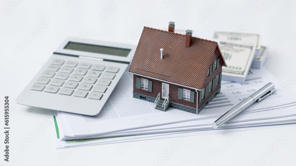 Model house, calculator, cash money and paperwork on a desk: real estate, home loan and investments concept Model house, calculator, cash money and paperwork on a desk: real estate, home loan and investments concept