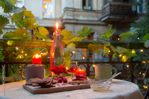 Romantic dinner table on balcony with candles, chocolates, fruits, honey and tea