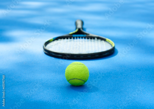 Yellow tennis ball is laying near professional racket on blue cort carpet. Made for playing tennis. Contrast image with satureted colors and shadows. Concept of sport equipment photo. photo