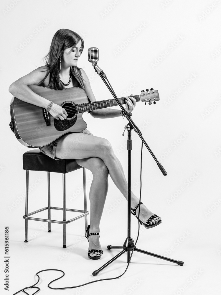 Photo of a young woman with long hair sitting on a stool playing an acoustic guitar over white background. Photo of a young woman with long hair sitting on a stool playing an acoustic guitar over white background.