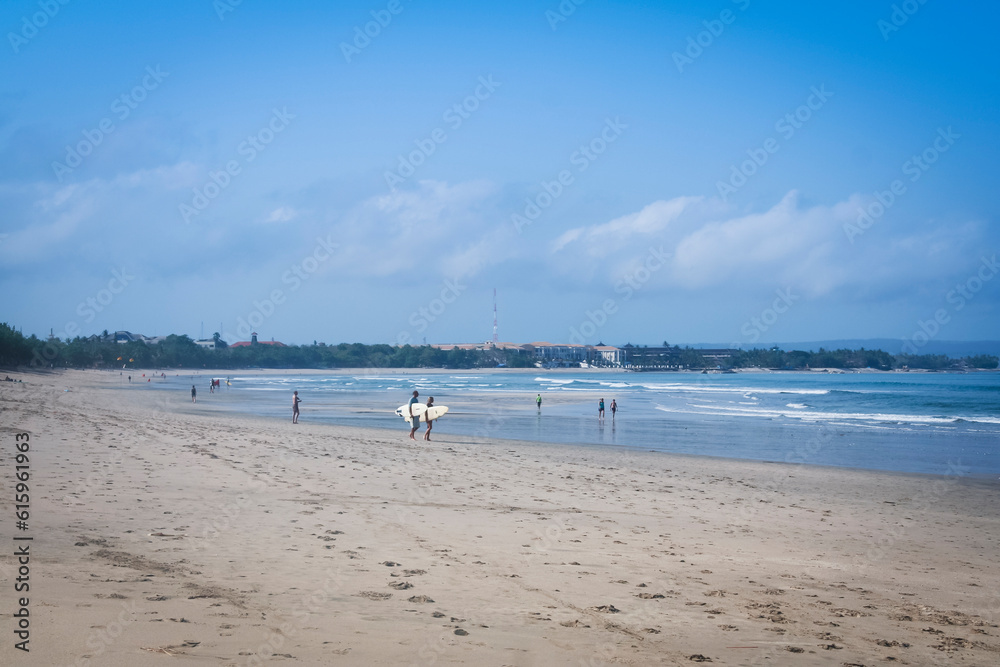 surfer couple carrying surfboards walking on kuta beach bali with denpasar behind
