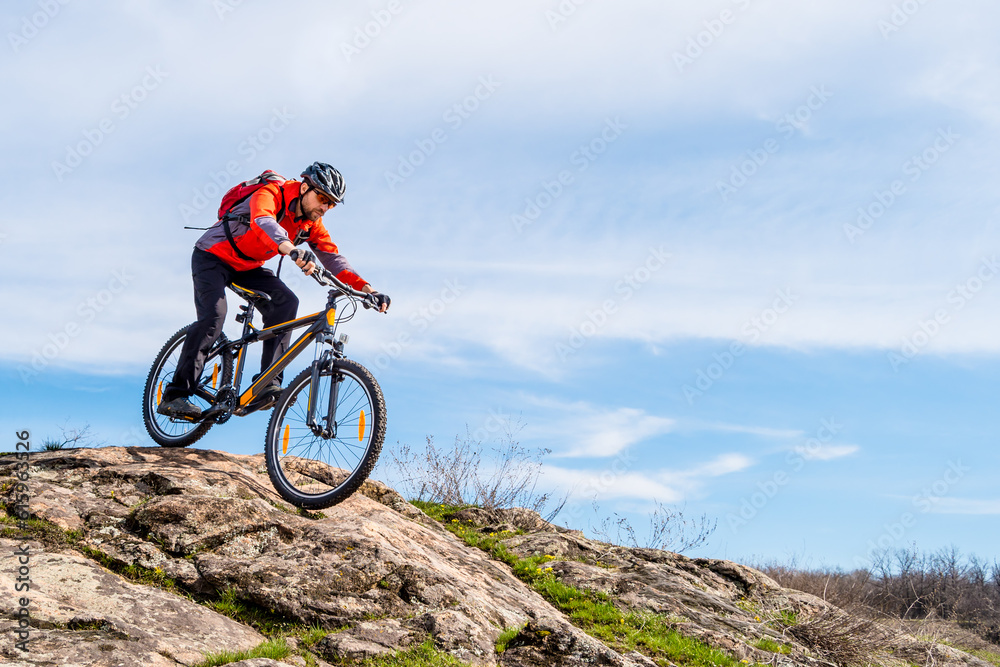 Cyclist in Red Jacket Riding the Mountain Bike Down Rocky Hill. Extreme Sport and Adventure Concept.