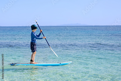 cheerful little boy enjoying stand up paddleboarding alone, active vacation concept, copy space on right