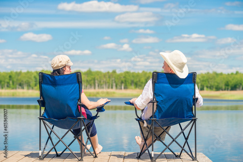 view from the back of a couple on chairs relaxes near a lake on a wooden pier