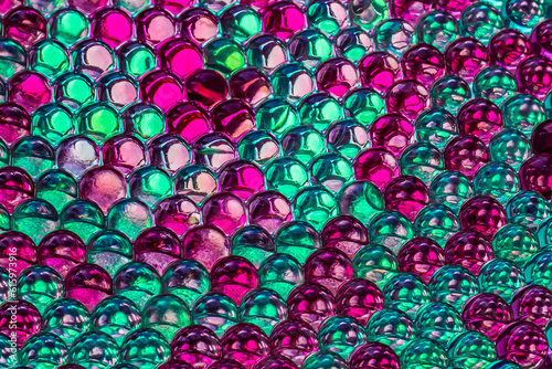 A beautiful horizontal bright colored texture of reflection of rainbow transparent hydrogel balls in green and purple color with reflection of blue sky and white clouds looks fantastic on the wet surf