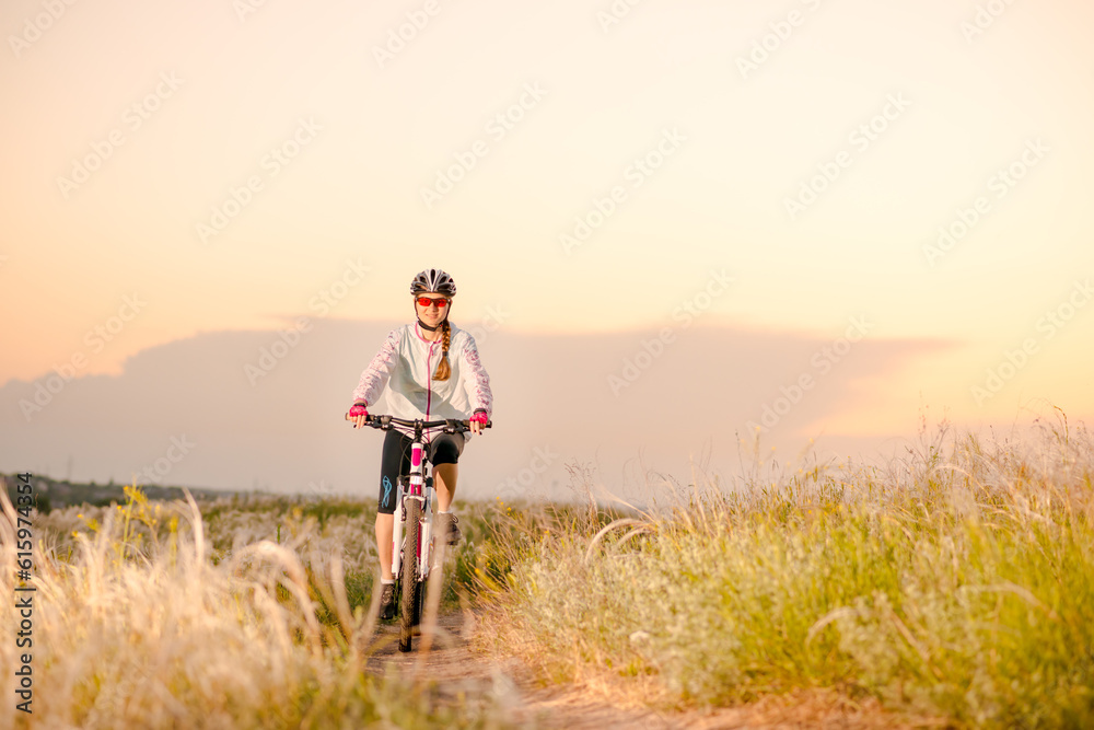 Young Woman Riding the Mountain Bikes in the Beautiful Field Full of Feather Grass at Sunset. Adventure and Travel Concept. Young Woman Riding the Mountain Bikes in the Beautiful Field Full of Feather Grass at Sunset. Adventure and Travel Concept.